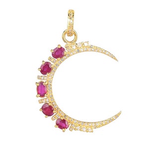 May include: A gold crescent moon pendant with a row of ruby red stones and smaller white stones around the edge.