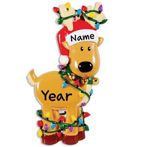 May include: A brown reindeer Christmas ornament with a red Santa hat, green and white garland, and colorful lights. The ornament has the text "Name" and "Year" on it.