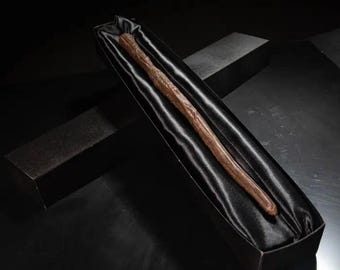 May include: A dark brown wooden wand in a black velvet-lined box. The box is closed and the wand is lying inside.