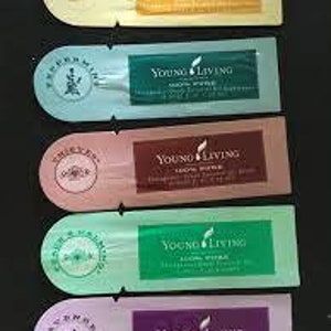 May include: Five Young Living essential oil sample packets. Each packet has a different color and scent: yellow (lemon), blue (peppermint), pink (thieves), green (stress away), and purple (lavender). Each packet has the Young Living logo and scent name.