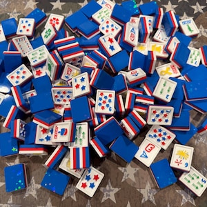 May include: A collection of blue, white, and red Mahjong tiles scattered across a surface. The tiles feature various symbols, numbers, and star patterns. The tiles are rectangular with a blue base and white tops with red and blue stripes.
