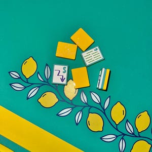May include: A teal background with yellow accents and several small, yellow, rectangular objects. A yellow and white lemon branch design is on the left. The image has a playful, summery vibe.