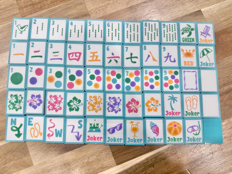 May include: A full set of Mahjong tiles with a turquoise border. The tiles display various symbols, numbers, and characters in green, orange, and purple. Some tiles have the words "Joker", "Green", and "Red".