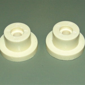 May include: Two off-white plastic furniture feet with a small round indentation in the center of each foot.