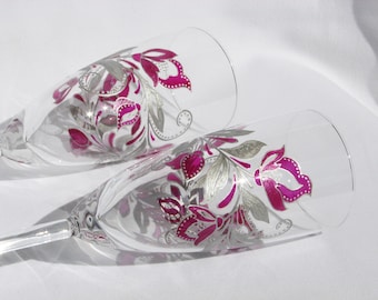 May include: Two champagne flutes with a floral design painted on the glass. The flowers are pink and silver.