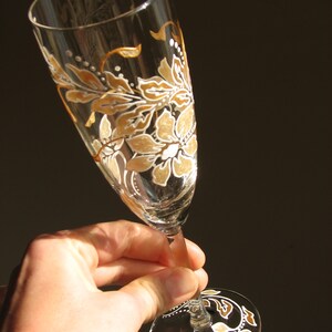 May include: A champagne flute with a hand-painted design of white and gold flowers and leaves.