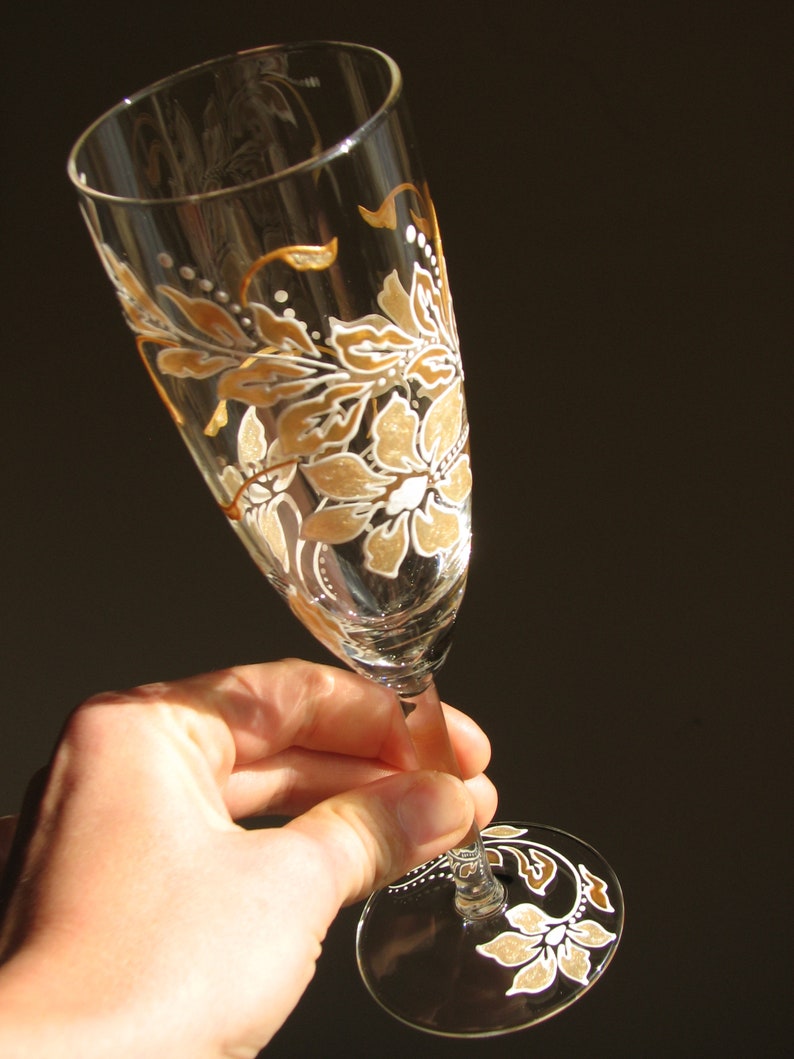 May include: A champagne flute with a hand-painted design of white and gold flowers and leaves.