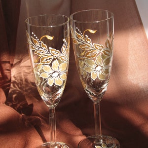 May include: Two champagne flutes with hand-painted floral designs in shades of brown and white. The flowers are stylized and have a vintage feel.