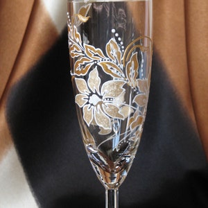 May include: A clear glass champagne flute with a gold and white floral design painted on the side.