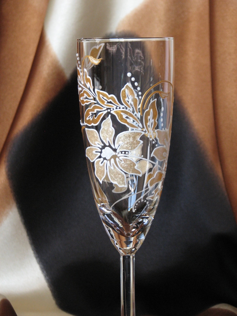 May include: A clear glass champagne flute with a gold and white floral design painted on the side.