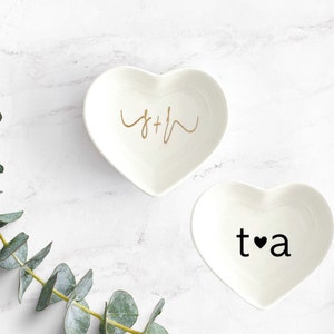 Puede incluir: Dos platos de cer&aacute;mica en forma de coraz&oacute;n blancos con letras doradas y negras. El primer plato dice "S+H" en letras doradas cursivas. El segundo plato dice "t&hearts;a" en letras negras.