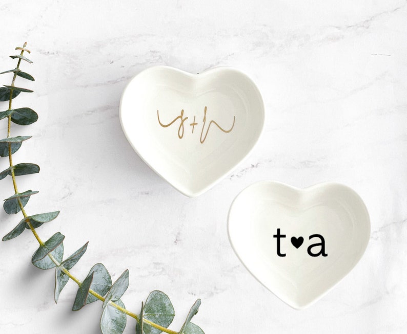 Puede incluir: Dos platos de cer&aacute;mica en forma de coraz&oacute;n blancos con letras doradas y negras. El primer plato dice "S+H" en letras doradas cursivas. El segundo plato dice "t&hearts;a" en letras negras.
