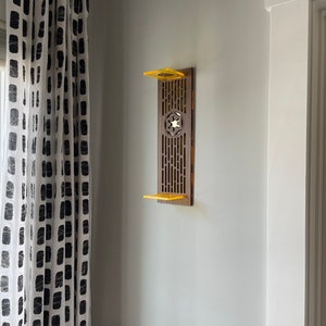 May include: A wooden wall shelf with a Star Wars themed design. The shelf is painted brown and has a yellow accent. The shelf is mounted on a white wall.