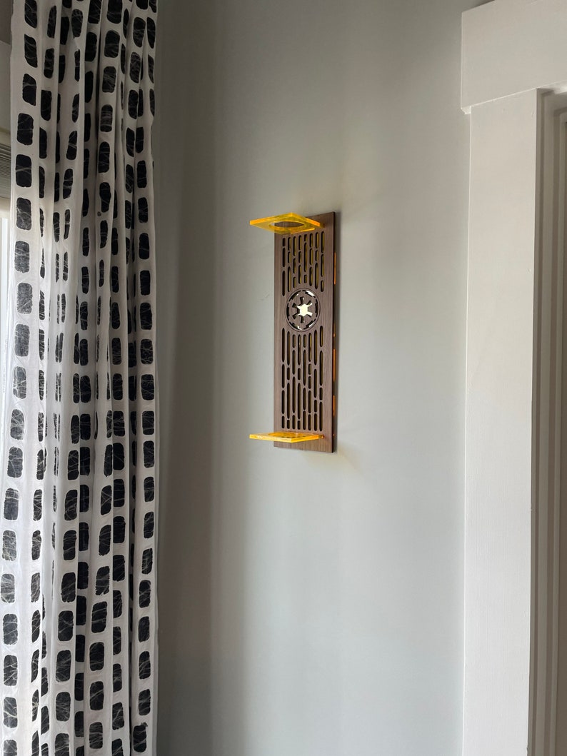 May include: A wooden wall shelf with a Star Wars themed design. The shelf is painted brown and has a yellow accent. The shelf is mounted on a white wall.