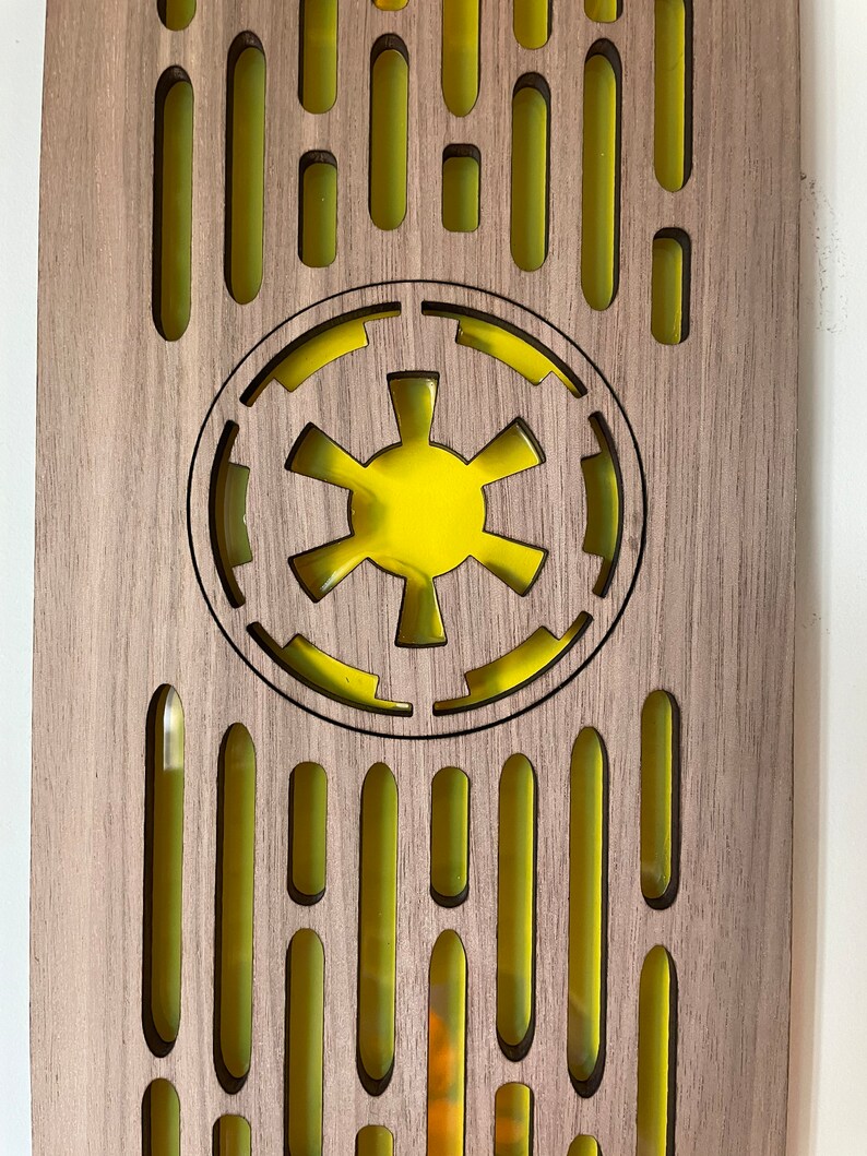 May include: A wooden plaque with a yellow Imperial symbol from Star Wars. The plaque has a repeating pattern of yellow ovals.