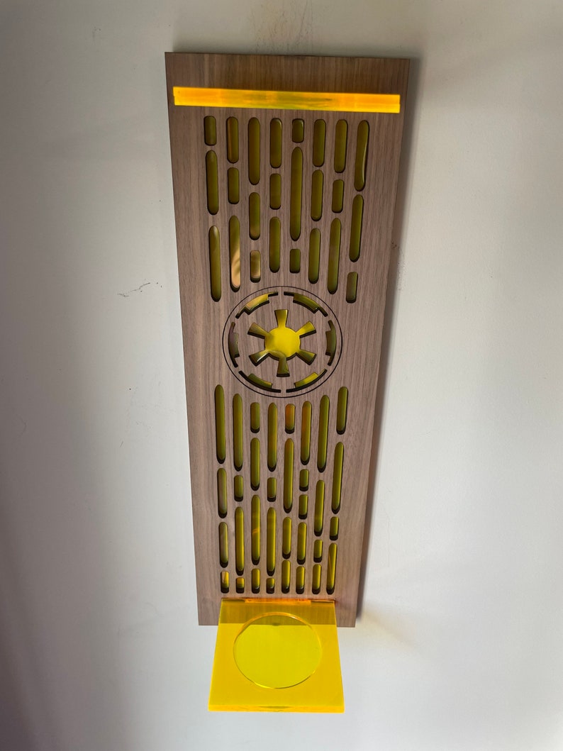 May include: A wooden wall decor with a yellow Imperial symbol and a yellow acrylic shelf. The decor has a repeating pattern of yellow ovals.