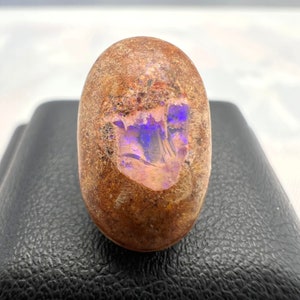 May include: An oval-shaped opal with a brown and orange exterior and a purple and pink iridescent flash.