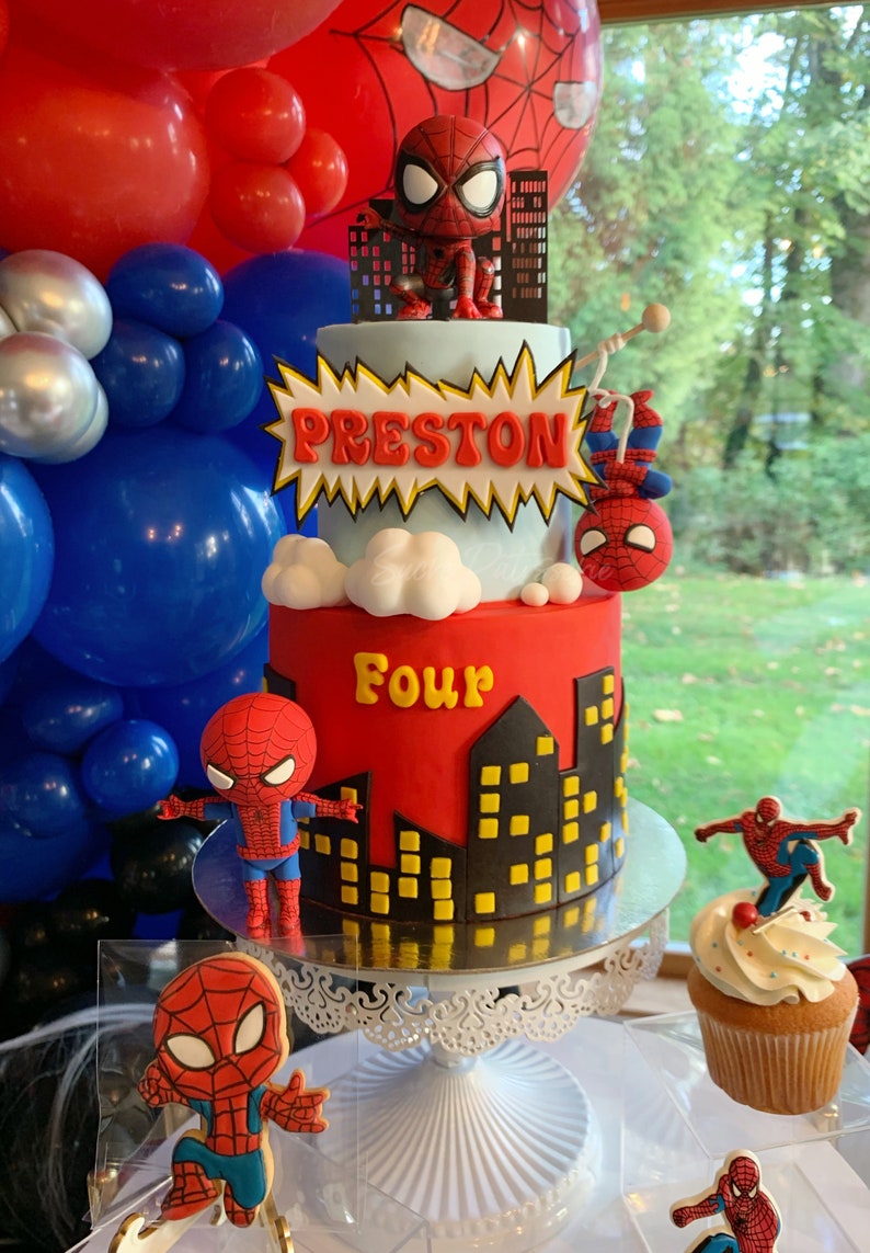 Puede incluir: Un pastel de cumplea&ntilde;os de dos pisos rojo y azul decorado con un tema de Spiderman. El pastel est&aacute; decorado con un personaje de Spiderman, un paisaje urbano y las palabras "Preston" y "Four".