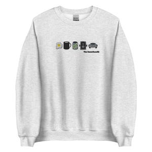 May include: Pale grey sweatshirt with a graphic design featuring an egg, a coffee mug, a can, a speaker, and a car. The text "The Ravenhood" is printed below the car.