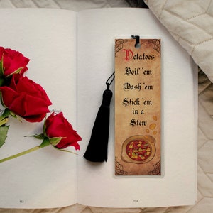 May include: A bookmark with a vintage design featuring a bowl of stew and the text "Potatoes Boil 'em Wash 'em Stick 'em in a Stew". The bookmark has a black tassel.