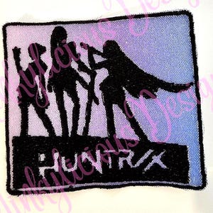 Puede incluir: Parche bordado con la silueta de tres figuras en un escenario, con la palabra "PHOENIX" en negrita. El fondo hace una transición de rosa a azul. El parche tiene un borde negro.