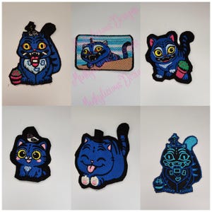 May include: A collection of six embroidered patches featuring cartoon cats in various poses. The cats are primarily blue with yellow eyes and black outlines. Some patches include additional colors like pink and green. The patches are on a white background.
