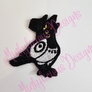May include: Black embroidered patch in the shape of a stylized bird. The bird has a white chest and eye, with yellow and red accents on its head. The patch is on a white background.