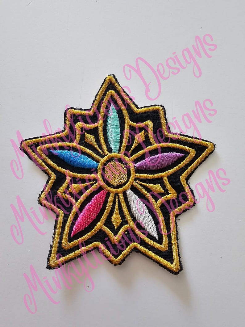 Puede incluir: Parche bordado con un dise&ntilde;o de estrella. El parche presenta un fondo negro con ribete dorado y acentos coloridos en azul, rosa, morado y turquesa. El centro tiene un dise&ntilde;o circular con detalles rosas y dorados.