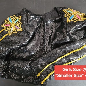 Puede incluir: Chaqueta negra con lentejuelas con adornos florales coloridos en los hombros y ribetes dorados. La chaqueta tiene una etiqueta de Talla de Ni&ntilde;a 7/8 y una etiqueta "Talla m&aacute;s peque&ntilde;a" 10 cm x 10 cm.