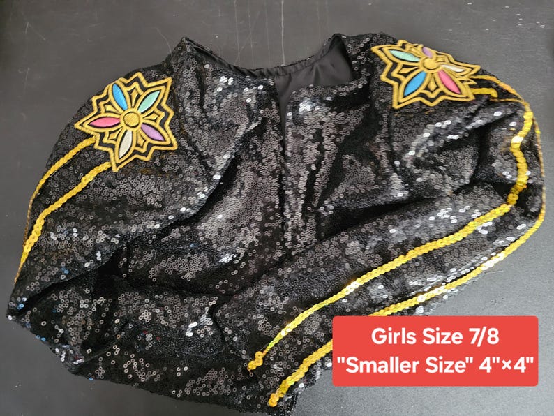 Puede incluir: Chaqueta negra con lentejuelas con adornos florales coloridos en los hombros y ribetes dorados. La chaqueta tiene una etiqueta de Talla de Ni&ntilde;a 7/8 y una etiqueta "Talla m&aacute;s peque&ntilde;a" 10 cm x 10 cm.