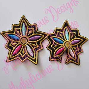 Puede incluir: Dos parches bordados en forma de estrella con fondo negro y ribete dorado. Los parches presentan un dise&ntilde;o floral colorido con acentos rosas, azules, morados y blancos. El texto "Minklylicious Designs" est&aacute; en el fondo.