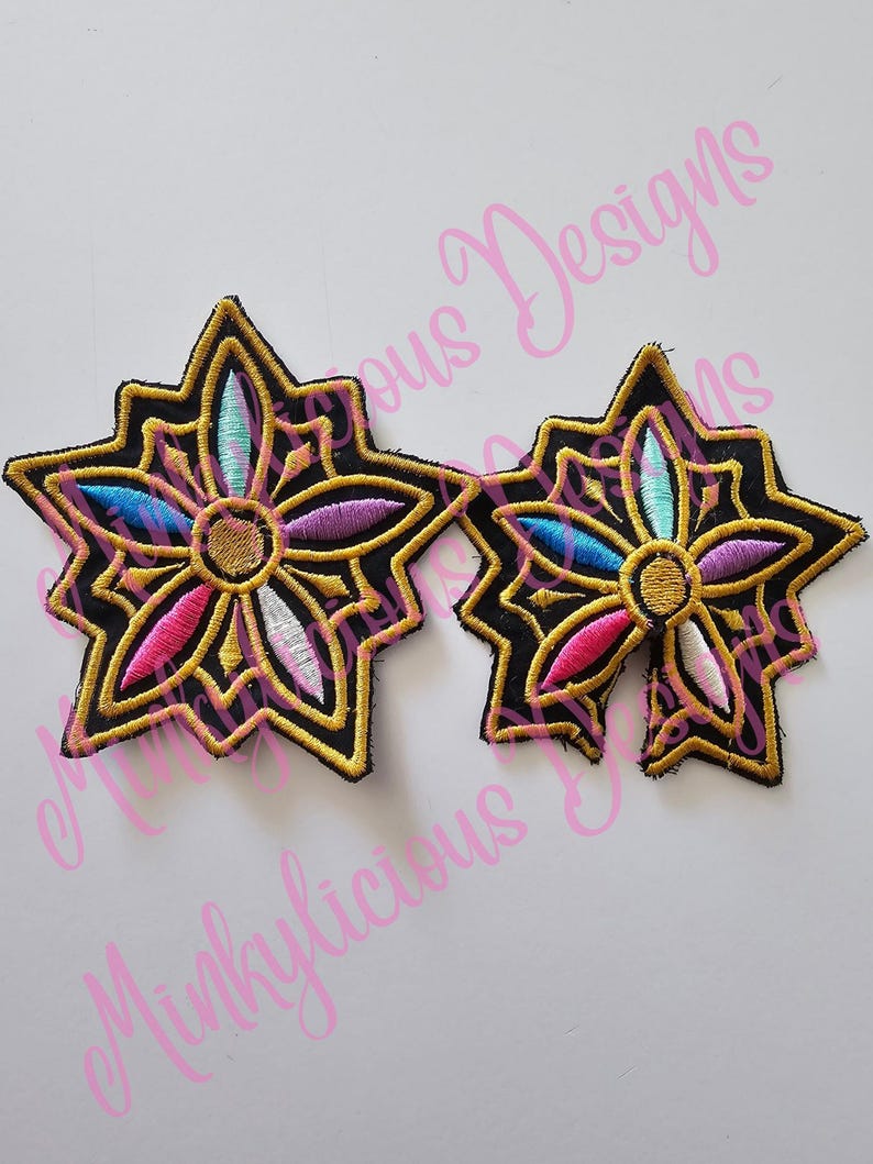 Puede incluir: Dos parches bordados en forma de estrella con fondo negro y ribete dorado. Los parches presentan un dise&ntilde;o floral colorido con acentos rosas, azules, morados y blancos. El texto "Minklylicious Designs" est&aacute; en el fondo.