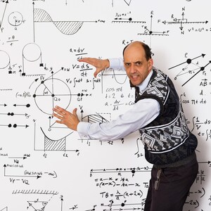 May include: A man in a patterned vest and white shirt gestures towards a whiteboard covered in mathematical equations and diagrams. The image conveys a theme of education and science.