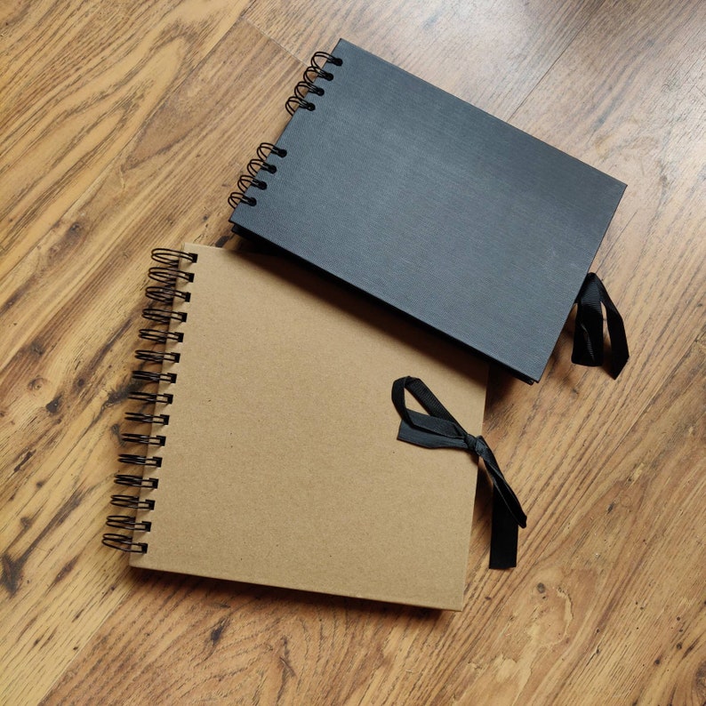 May include: Two spiral bound photo albums, one black and one brown, with black ribbon ties.