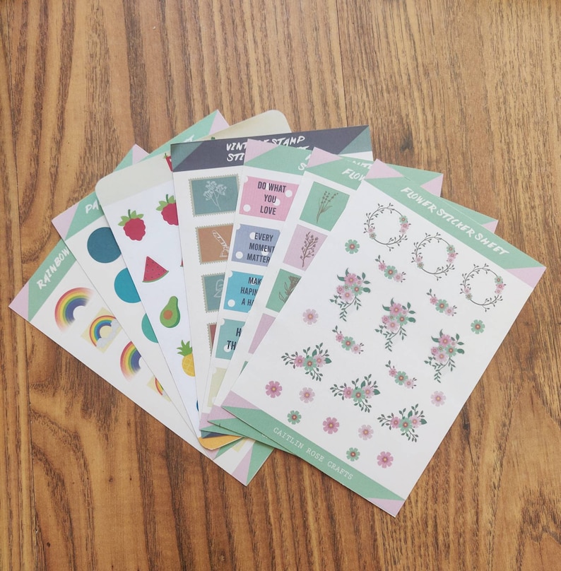 K&ouml;nnte beinhalten: Ein Set mit sechs Stickerb&ouml;gen mit verschiedenen Designs. Die B&ouml;gen enthalten einen Regenbogen, Fr&uuml;chte, Blumen und Briefmarken mit motivierenden Zitaten. Die B&ouml;gen sind auf wei&szlig;em Papier mit einem hellgr&uuml;nen Rand gedruckt.