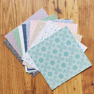 May include: A stack of patterned paper sheets in various shades of blue, pink, and green. The top sheet features a teal and white mandala design.