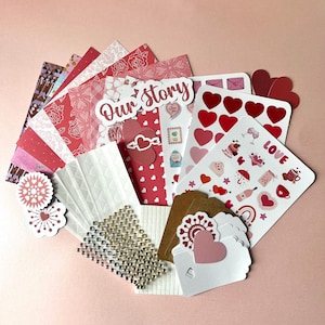 May include: A collection of craft supplies featuring patterned paper sheets in shades of red and pink, sticker sheets with heart and love-themed icons, a sheet of adhesive rhinestones, and several blank white and brown cardstock gift tags.