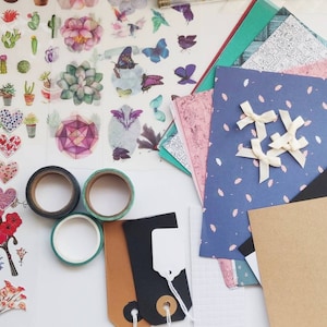 May include: A collection of craft supplies including colorful patterned paper, washi tape, stickers, and embellishments. There are also two black and white tags with string.