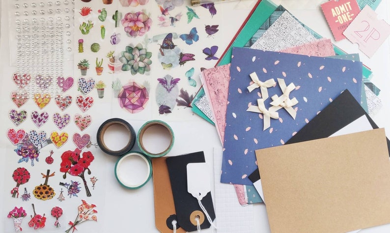 May include: A collection of craft supplies including colorful patterned paper, washi tape, stickers, and embellishments. There are also two black and white tags with string.