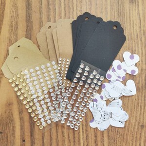 May include: A set of craft supplies including brown and black paper tags, clear heart-shaped rhinestones, and paper hearts with musical notes and purple accents.