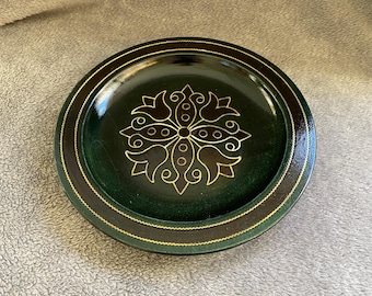 May include: A green wooden plate with a gold and black geometric design in the center. The plate has a dark brown rim with a gold trim.