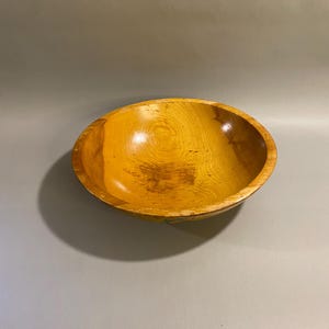 May include: A wooden bowl with a warm, golden-yellow hue. The bowl has a smooth, polished finish and a rounded shape. The wood grain is visible, adding to the natural aesthetic. The bowl is empty and appears to be in good condition.