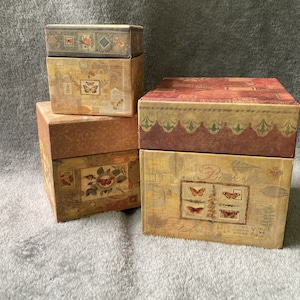 May include: Set of four decorative boxes with a vintage floral and butterfly design. The boxes are stacked on top of each other and have a brown, red, and cream color scheme.