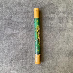 May include: A cylindrical, hand-painted bamboo didgeridoo. The instrument features a green body with yellow and white dot patterns and a spiral design. The ends are a natural bamboo color.