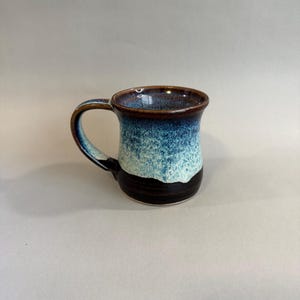 May include: A ceramic mug with a dark brown rim and handle. The mug transitions from a dark brown base to a blue and white speckled middle, and a dark brown rim. The mug is designed for hot beverages.