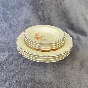 May include: A set of five white ceramic plates with a floral design. The plates are stacked on top of each other, with the largest plate on the bottom and the smallest plate on top. The plates have a scalloped edge and a black trim.