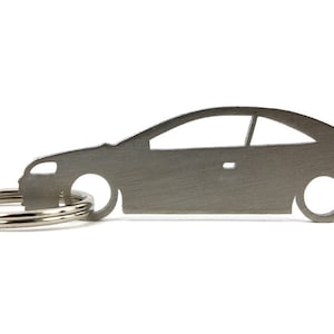Może przedstawiać: Srebrny metalowy brelok do kluczy w kształcie samochodu. Brelok ma srebrny metalowy pierścień.