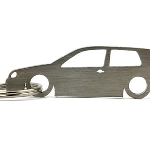 Puede incluir: Un llavero de metal plateado con forma de coche Volkswagen Golf. El llavero tiene un acabado de metal cepillado y un anillo de llave plateado.