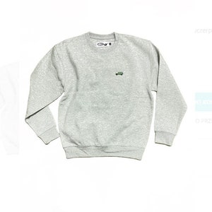 May include: A grey sweatshirt with a small green car embroidered on the front. The sweatshirt has a crew neck and long sleeves.
