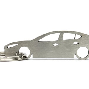 Puede incluir: Un llavero de metal plateado con forma de coche. El llavero tiene un anillo para llaves sujeto a la parte delantera.